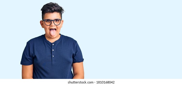 Kleiner Junge, der lockere Kleidung trägt und eine Brille hält Zunge mit lustigem Ausdruck glücklich. Emotionskonzept. 