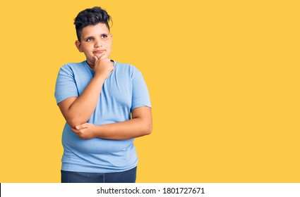 Little Boy Kid Wearing Sports Workout Clothes With Hand On Chin Thinking About Question, Pensive Expression. Smiling With Thoughtful Face. Doubt Concept. 