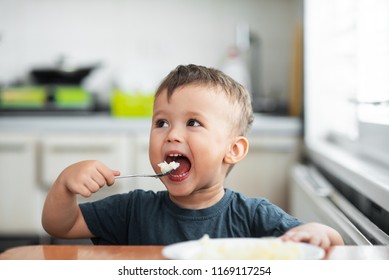 The Little Boy In The Kitchen Eagerly Eating Rice With A Spoon Independently