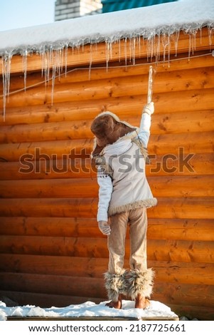 A little boy knocks icicles off the roof of a house. Cold winter weather.