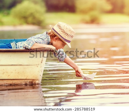 Little boy launch paper ship from old boat on the lake