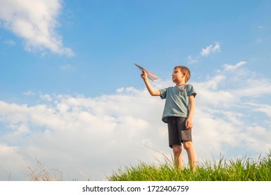 Little Boy Launches A Paper Plane Into The Air. Child Launches A Paper Plane. Happy Kid Playing With Paper Airplane.