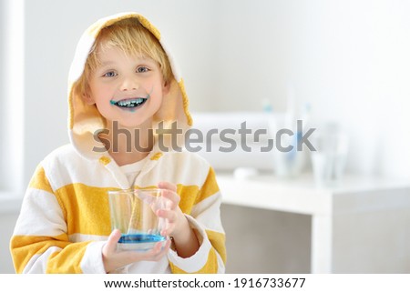 Little boy is learning carefully brush teeth. Child using liquid for disclosing plaque. Teaching children proper oral hygiene. Dental medicine and healthcare for kids.