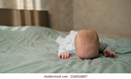 A Little Boy Lies On The Bed And Tries To Roll Over. A Cute Baby Lies On The Bed And Tries To Roll Over.