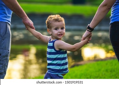 Little Boy Looking Back While Walking Holding Hands With His Parents.