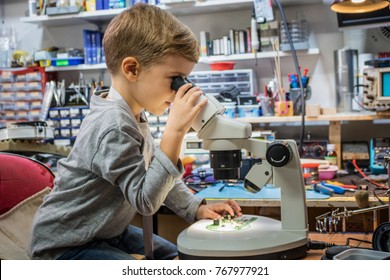 Little Boy Looking Through Microscope While Examining Circuit Board In IT Laboratory During School Science Project.