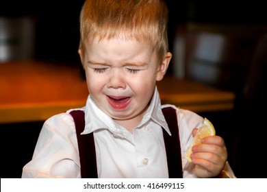 A little boy makes an awful face after tasting a sour lemon.