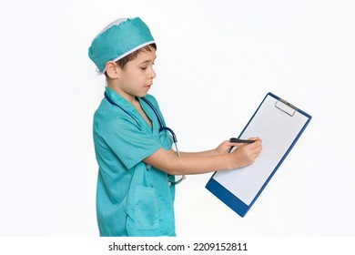 Little Boy In Medical Uniform Character Holds Clipboard And Writing Diagnosis. Serious Swarthy Boy Writes Down A Treatment Plan On Clip-on Tablet, Isolated On White