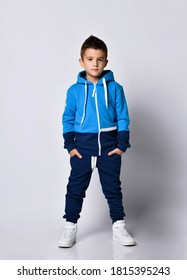 Little boy model wearing sports tracksuit with sweatshirt and pants studio portrait isolated on gray background. Male child posing for camera with hands in pocket. Autumn winter sport children fashion