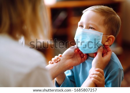 Little boy and mom in medical mask. Mother puts on her baby sterile medical mask. Child, wearing face mask, protect from infection of virus, pandemic, outbreak and epidemic of disease on quarantine.