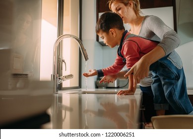 Little boy with mother washing hands in kitchen sink. Woman helping her son to wash hands in kitchen sink after cooking.