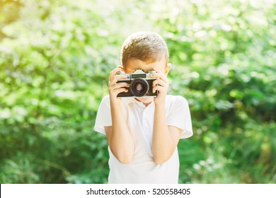 Little Boy With An Old Camera Shooting Outdoor. Kid Taking A Photo Using A Vintage Retro Film Cam. Green Summer Field.