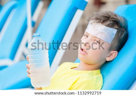 Little boy on the beach with a sunstroke holds a bottle of water