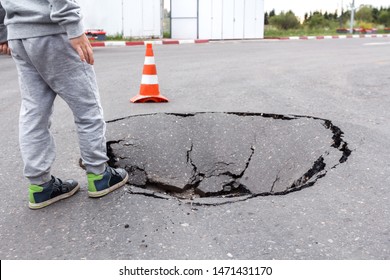 A Little Boy On The Edge Of A Large Pit In The Road Surface. A Hole In The Pavement. Failure In The Ground. The Need For Highway Repair. The Emergency Situation In The City. Danger Of Injury Outdoors.