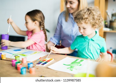 Little boy with paintbrush drawing his picture with paints together with his sister and mother helping to them - Shutterstock ID 1139987585