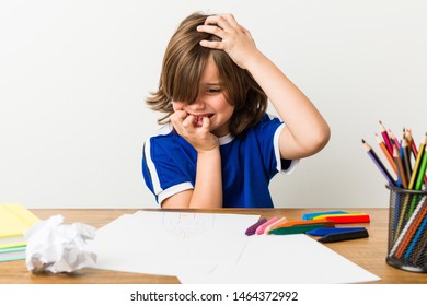 Little boy painting and doing homeworks on his desk biting fingernails, nervous and very anxious.