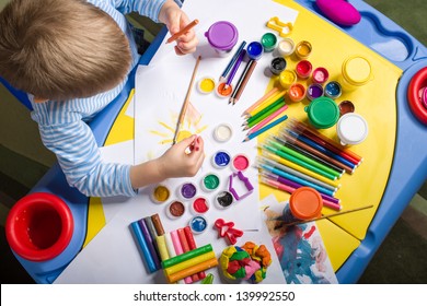 Little Boy Painting At The Table With Art Supplies, Top View