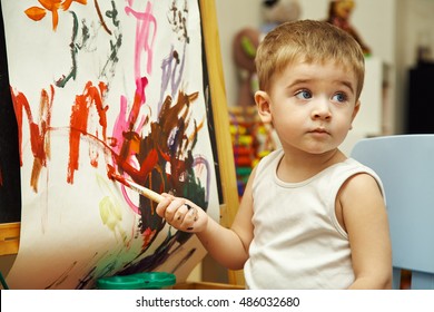 Little Boy Paints A On An Easel With A Brush. Painting Child