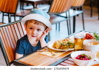 Little Boy In Panama Hat Talking On The Mobile Phone At The Dinner Table