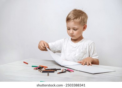 A little boy passionately draws with colored pencils in a sketchbook while sitting at a table in his childhood room. Blurred background. - Powered by Shutterstock