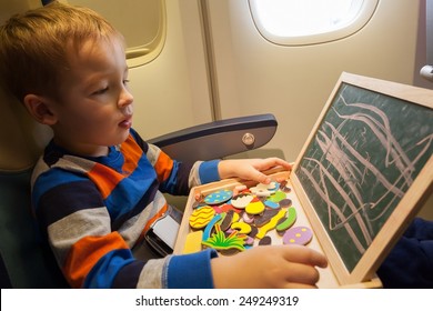 Little Boy In The Plane Drawing On Small Board With Chalk. Entertainment During Flight