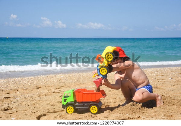 Little boy play in sand on beach. Child playing
with a track and excavator in
sand