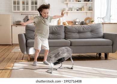 Little boy play with strong wind blow from ventilator or industrial fan at home in cozy living room. Small kid alone with retro air conditioner enjoy refreshing fresh breeze. Child has fun with cooler