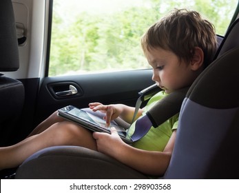 Little Boy Playing With Concentration On Computer Tablet Goes Child Seat In The Car