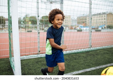 Little Boy Playing Football. African American Schoolboy At Stadium. Young Kids Running Outside. Happy Black Children Practicing Soccer. Training At Field With Ball. Exercise And Healthy Lifestyle