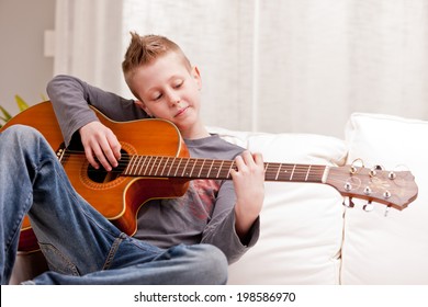 little boy playing guitar on a sofa in his living room - Powered by Shutterstock