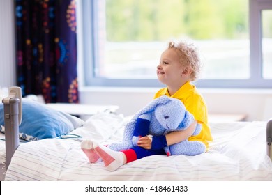 Little Boy Playing With His Toy In Bed In Hospital Room. Child With IV Tube And Pulse Oximeter In Modern Clinic. Kid Recovering From Sickness. Post Operative Care At Children Station. Kids Health Care