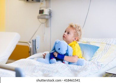 Little Boy Playing With His Toy In Bed In Hospital Room. Child With IV Tube And Pulse Oximeter In Modern Clinic. Kid Recovering From Sickness. Post Operative Care At Children Station. Kids Health Care