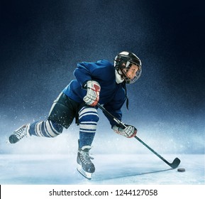 Little Boy Playing Ice Hockey At Arena. A Hockey Player In Uniform With Equipment Over A Blue Background. The Athlete, Child, Sport, Action Concept