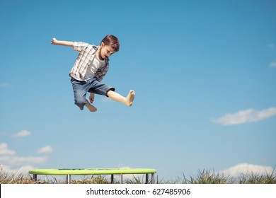 Little boy playing on the field at the day time. People having fun outdoors. He jumping on trampoline on the lawn. Concept of friendly family. - Powered by Shutterstock