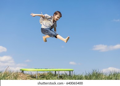 Little boy playing on the field at the day time. People having fun outdoors. He jumping on trampoline on the lawn. Concept of friendly family. - Powered by Shutterstock