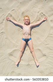 Little Boy Playing On Sea Beach Making An Angel On A Yellow Sand.