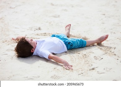 Little Boy Playing On Tropical Beach Making An Angel On White Sand