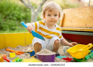 A little boy playing in the sandbox at the playground outdoors. Toddler playing with sand molds and making mudpies. Outdoor creative activities for kids. - Powered by Shutterstock