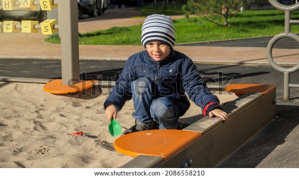 Little boy playing in sandpit with toy plastic\
shovel in park