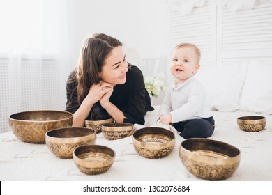 Little boy playing with Tibetan singing bowls sitting on the bed. Sound therapy for the baby. Toning.