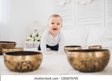 Little boy playing with Tibetan singing bowls sitting on the bed. Sound therapy for the baby. Toning.