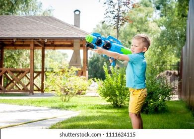 Little Boy Playing Water Gun In Backyard In Summer Vacations. Kid Has Fun With 
Blaster.