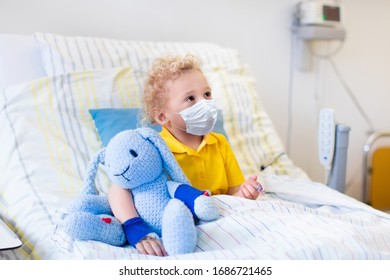 Little Boy Playing Wearing Face Mask With His Toy In Bed In Hospital Room. Child With IV Tube And Pulse Oximeter In Clinic. Kid Recovering From Coronavirus. Corona Virus Outbreak. Patient In Kids Ward