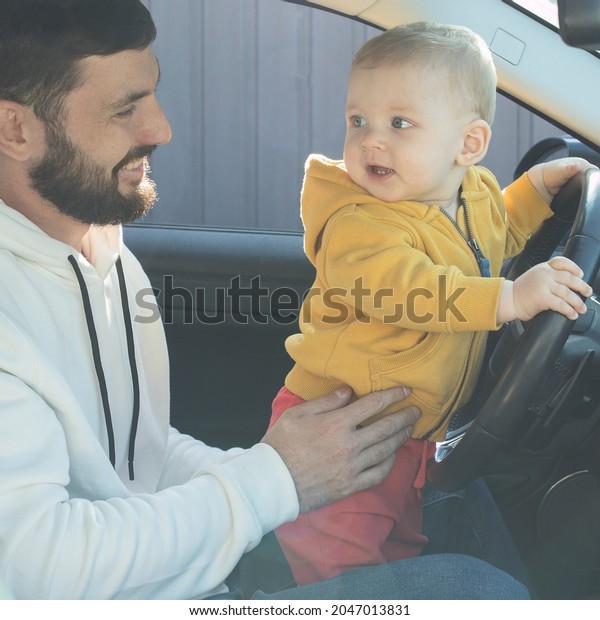 Little boy plays in the car, stands in front seat,\
holding wheel. Dad supports child. Father with baby in the car.\
Life insurance concept, auto insurance, parenthood, happy family,\
trip. Soft focus.