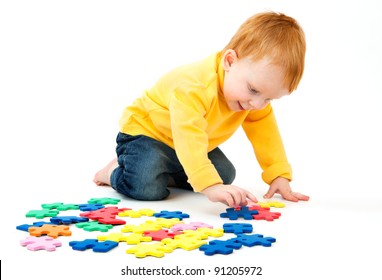 Little boy plays with a multi colored puzzle a white background