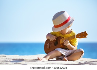 Little boy plays on Hawaiian guitar or ukulele at sea beach background. Space for text