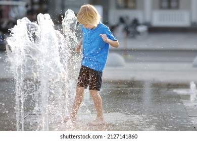 Little boy plays in the square between the water jets in the dry fountain at sunny summer day. Active summer leisure for kids in the city.