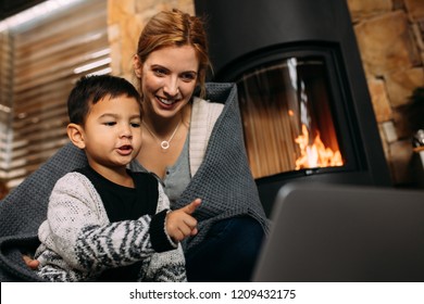 Little boy pointing at laptop while sitting with mother near fireplace at home. Mother and son looking at something interesting on laptop computer in living room. - Powered by Shutterstock