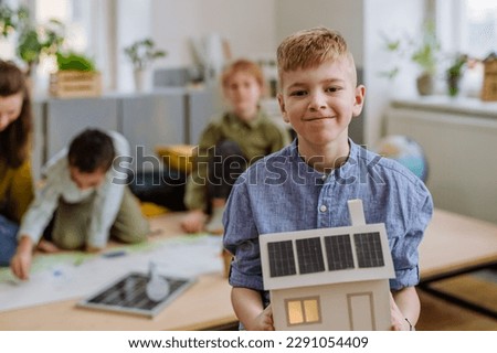 Little boy posing with model of house with solar system during a school lesson.