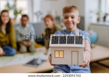 Little boy posing with model of house with solar system during a school lesson.